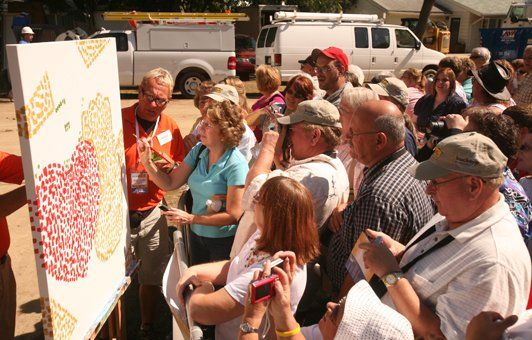 People watch an artist paint on a large canvas outdoors.