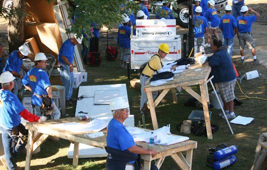 Group of volunteers in blue shirts and hard hats working at a construction site outdoors.