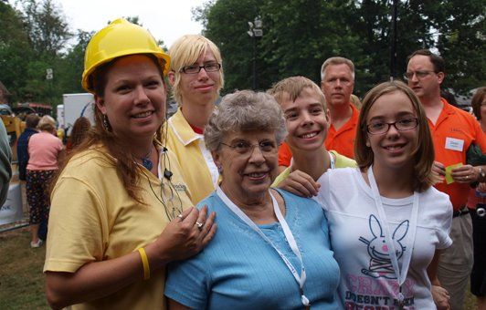 Group of people smiling, some wearing yellow shirts and a hard hat, outside.