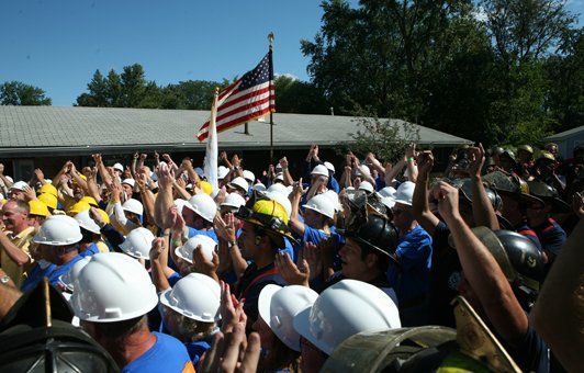 People in hard hats raise arms toward American flag.