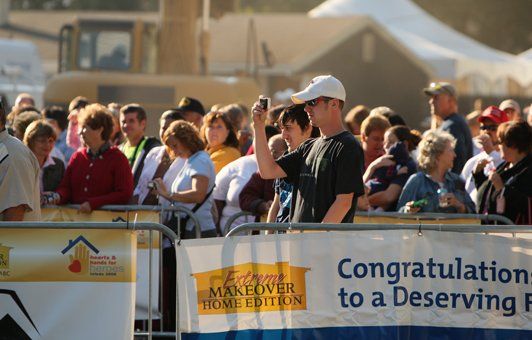 Man taking photo with phone in crowd behind a barricade with 