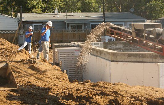 Construction workers filling a concrete structure with gravel from a conveyor belt.