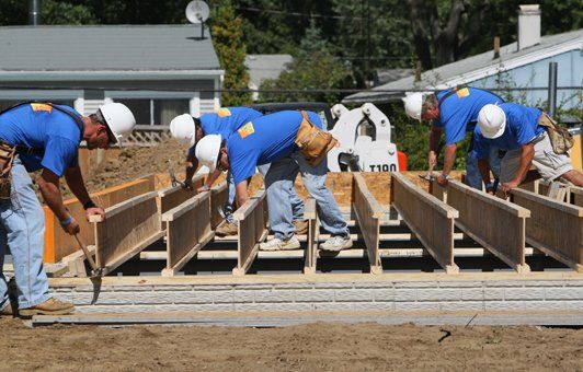 Construction workers in blue shirts and hard hats, building a structure outdoors.