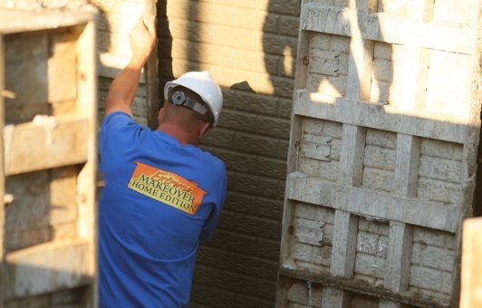 Construction worker in blue shirt and hard hat working on concrete forms.