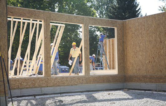 Construction workers framing a wall with window openings. Building interior, gray foundation, OSB sheathing.