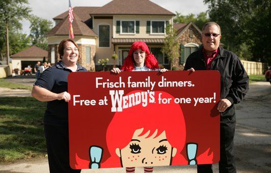 Three people holding a Wendy's sign in front of a house: Offers Frisch family dinners free at Wendy's for a year.