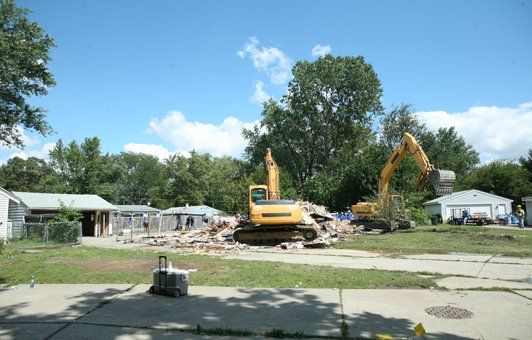 Two excavators demolish buildings under a blue sky.