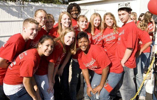 Group of people in red shirts smiling, posing outdoors.