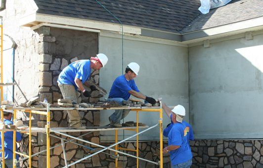 Construction workers installing stone veneer on a building exterior, using scaffolding.
