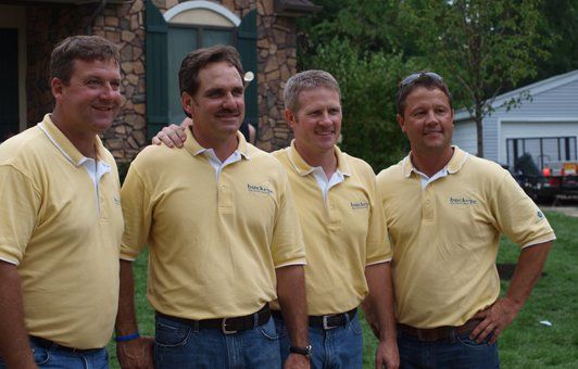 Four men in yellow shirts and jeans standing outdoors, posing for a photo.