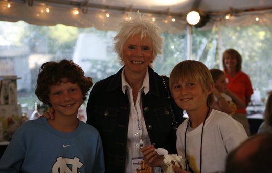 Woman with white hair poses with two smiling boys outdoors.