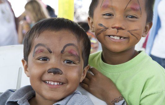 Two children with face paint smiling. One is brown, the other is green.