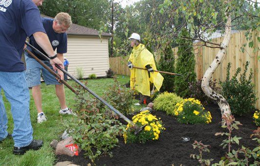 People landscaping a garden; one in yellow raincoat.