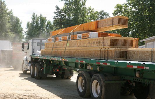 Flatbed truck carrying stacks of lumber on a sunny day.