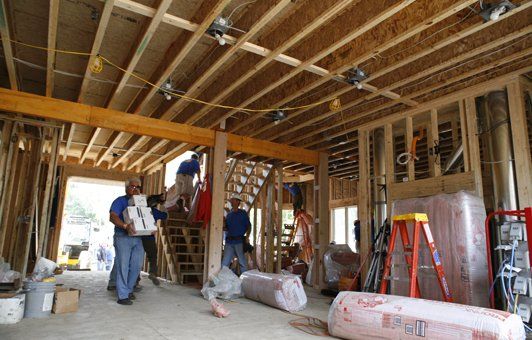 Construction workers installing insulation in a wood-framed building's interior.