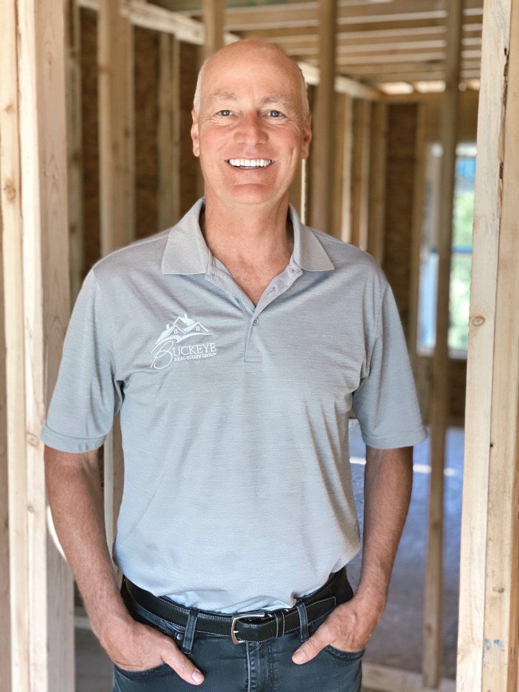 A man in a gray shirt is standing in front of a house under construction.