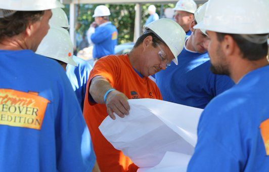 Construction workers in hard hats reviewing blueprints outdoors.