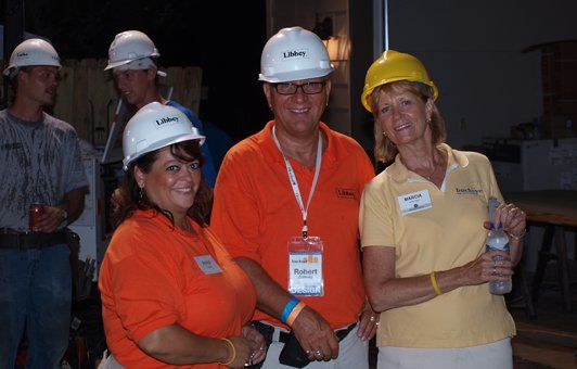 Group of people in hard hats and orange shirts, posing for a photo at a construction site.