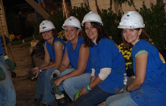 Four people in blue shirts and hard hats sitting outdoors.