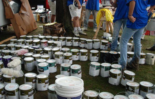 Group of people preparing to paint, with many paint cans on the grass.