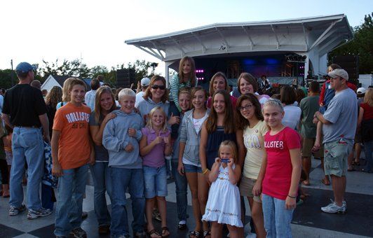 Group of people pose in front of a stage with a crowd; a fair-skinned, light-haired group smiling at the camera.