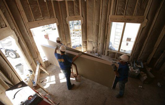 Construction workers carrying drywall inside a building under construction.