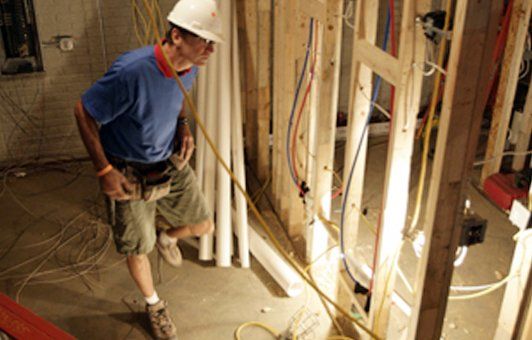 Construction worker in hard hat inspecting wiring in a partially built wall, indoors.