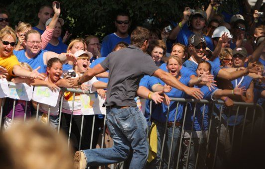 Man running towards a crowd of people behind a metal barrier, many wearing blue shirts.