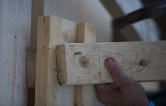 Close-up of a hand holding a wooden beam, hammering it into a structure's frame.