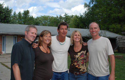 Five people smiling, arms around each other, standing outside a building.