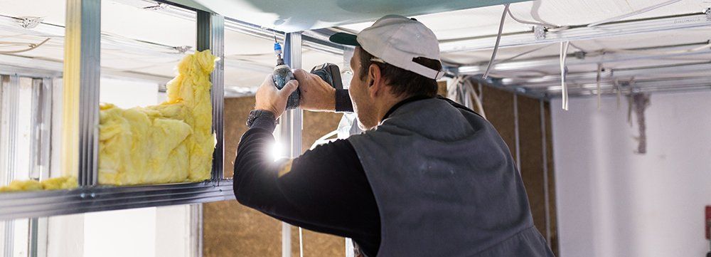 man with drill fixing drywall on ceiling next to insulation