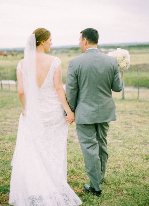 a bride and groom are walking in a field holding hands .