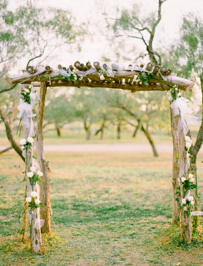 a wooden arch decorated with flowers and ribbons is in the middle of a field .