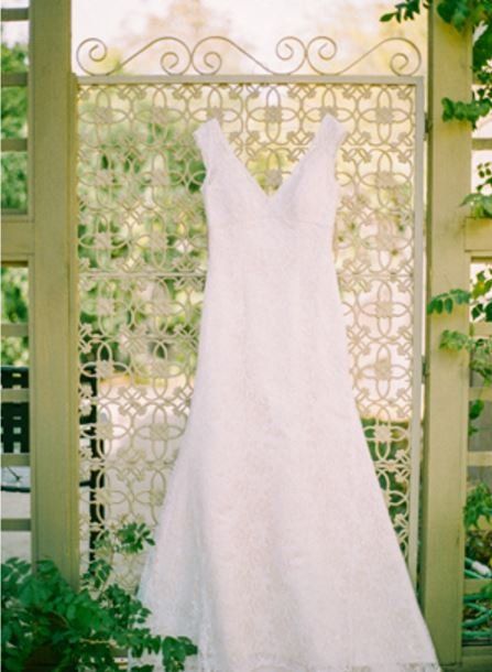 a white wedding dress is hanging on a gate