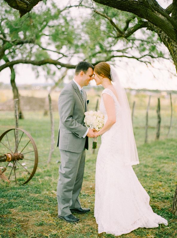 a bride and groom are standing under a tree holding hands