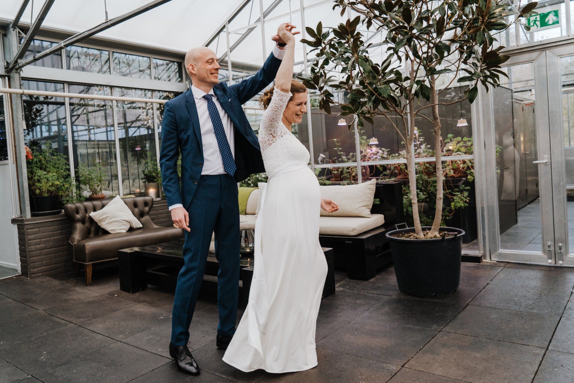 Een zwangere bruid en bruidegom dansen in een kas.