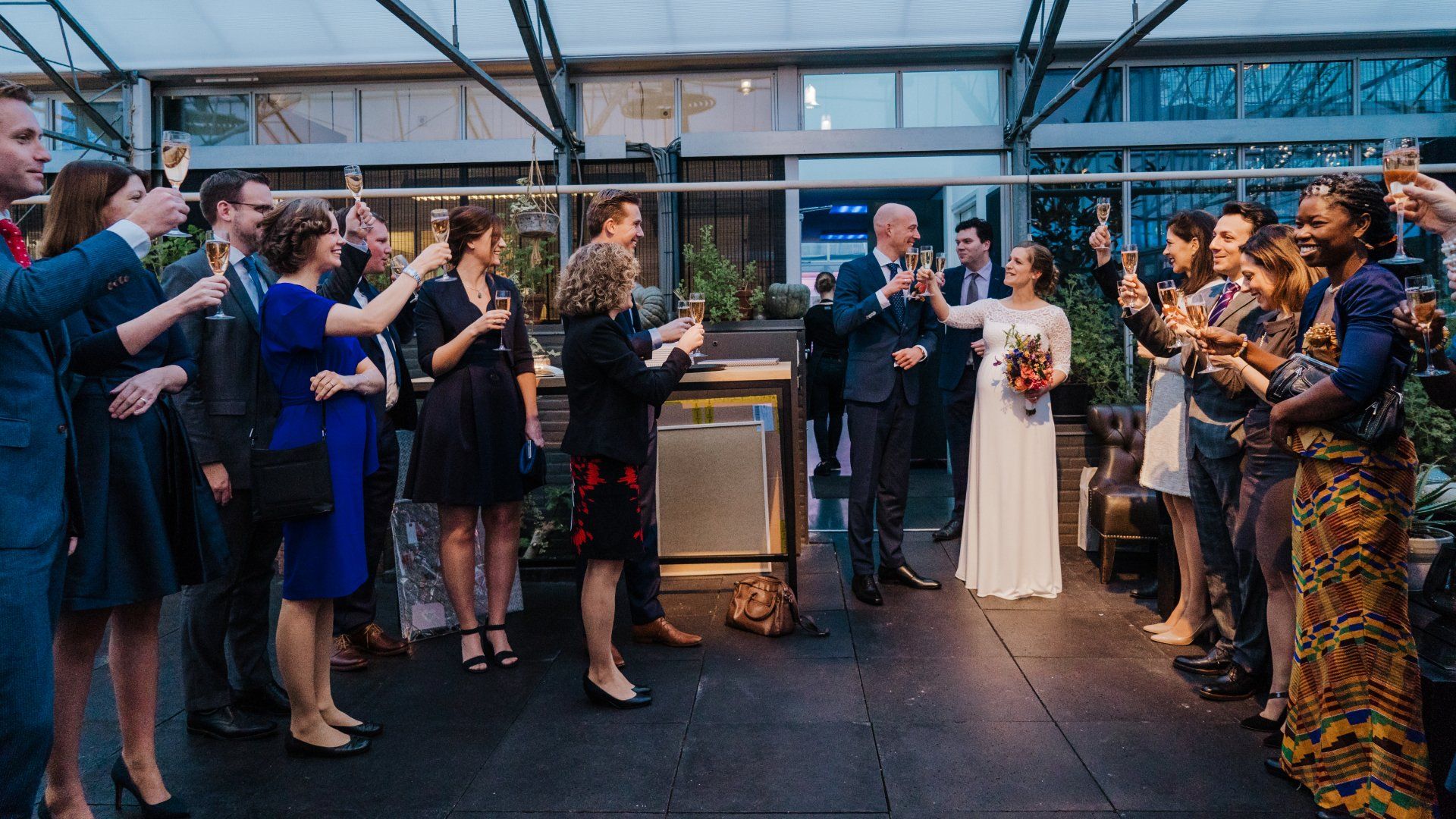 Een groep mensen staat rond een bruidspaar en brengt een toost uit met champagne.