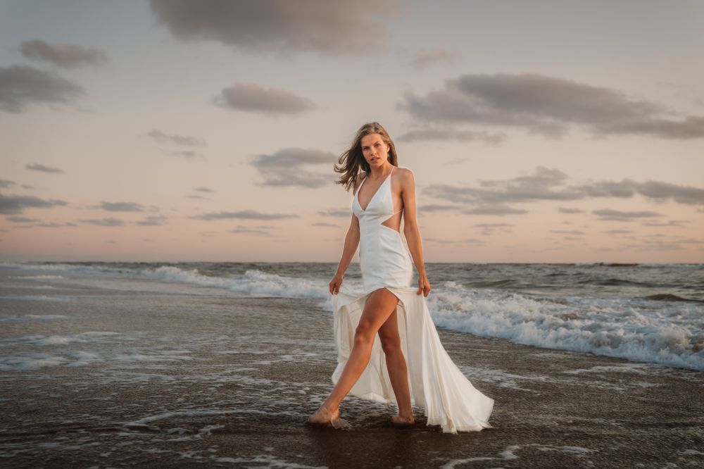Een vrouw in een witte jurk loopt op het strand.