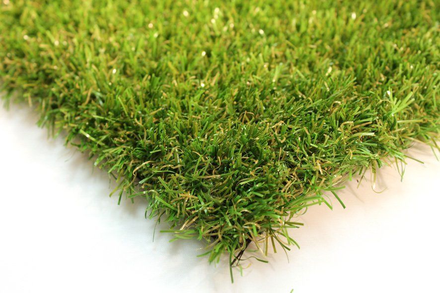 Close-up van een vierkant kunstgrasveld; groene grassprieten met bruine ondertonen op een witte ondergrond.