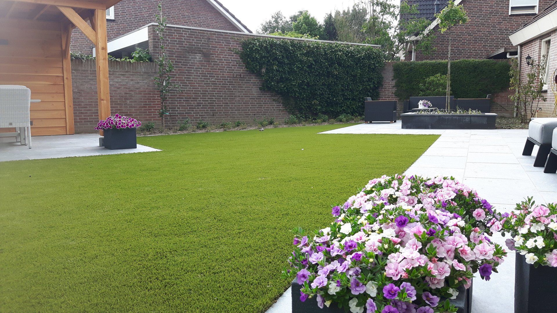 Achtertuin met groen gazon, bloempotten en stenen terras.