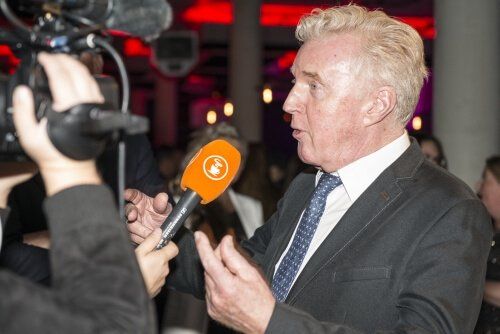 Een man in pak en stropdas praat in een oranje microfoon