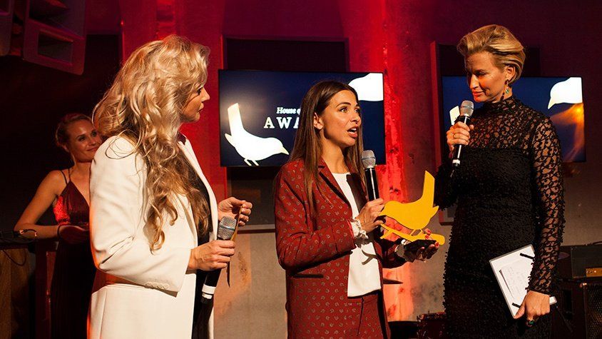Drie vrouwen staan op een podium met microfoons in hun handen.