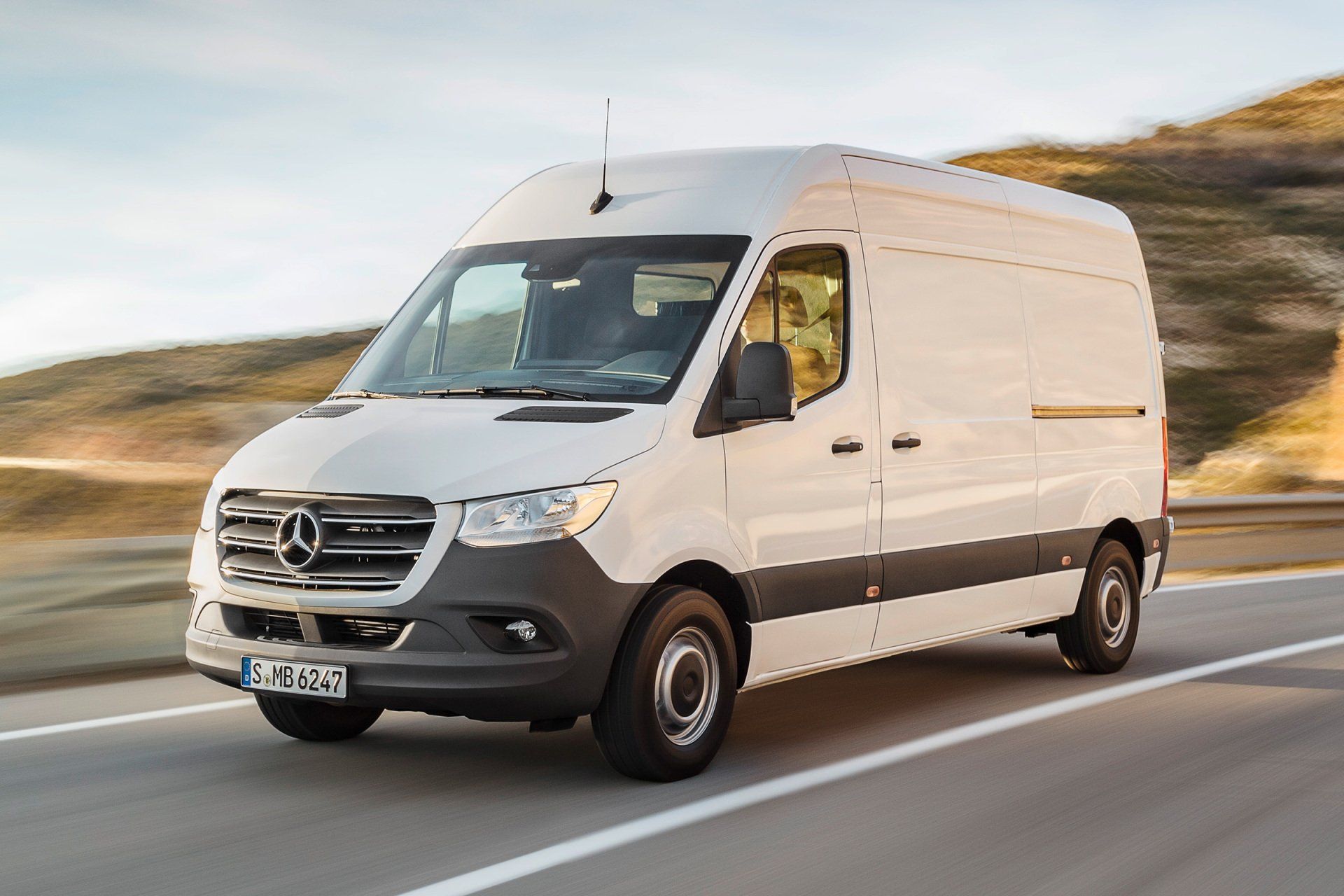 A white mercedes benz sprinter van is driving down a road.