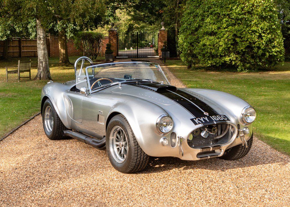 A silver sports car is parked on a gravel driveway.