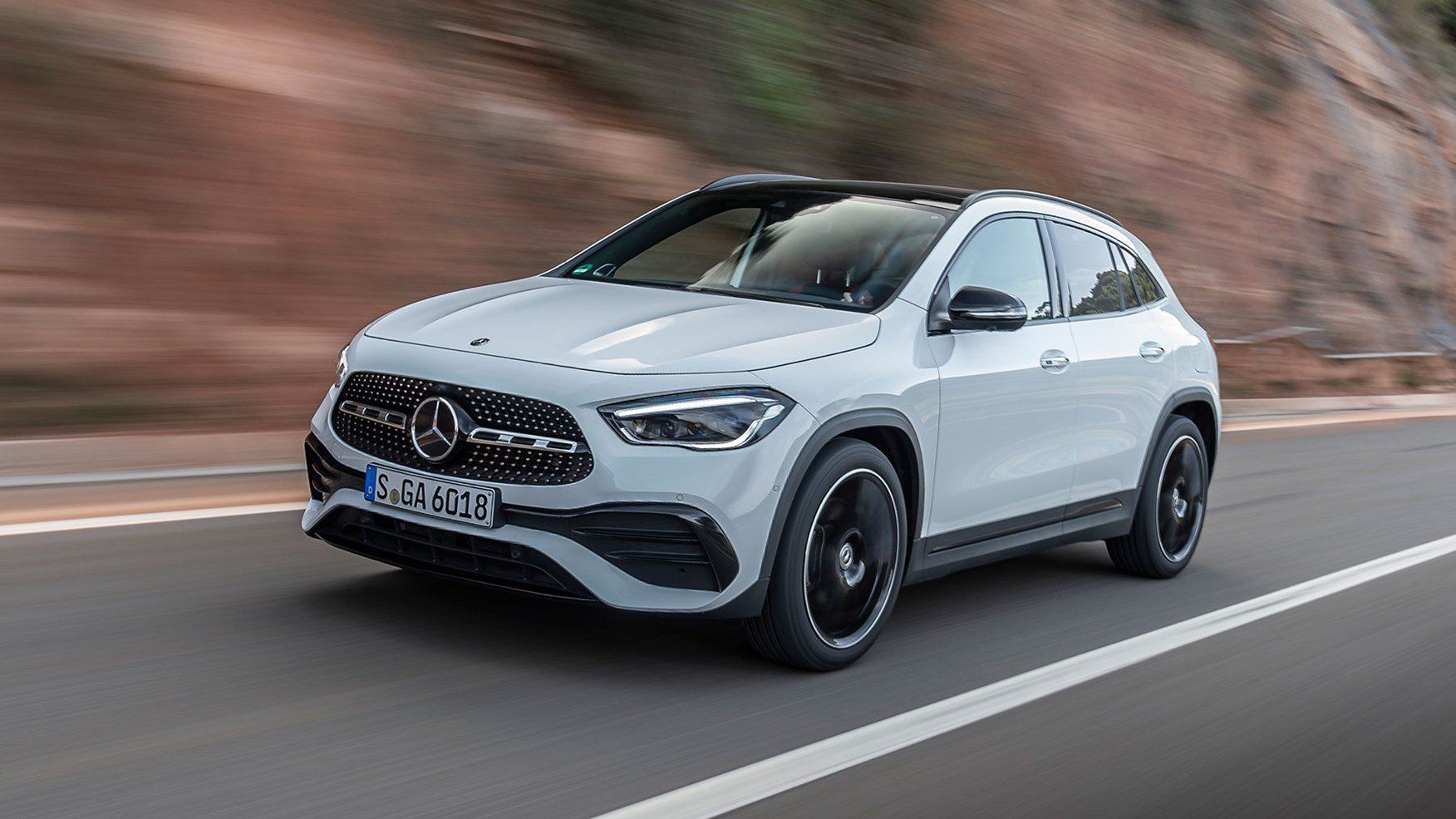 A white mercedes benz gla is driving down a road.