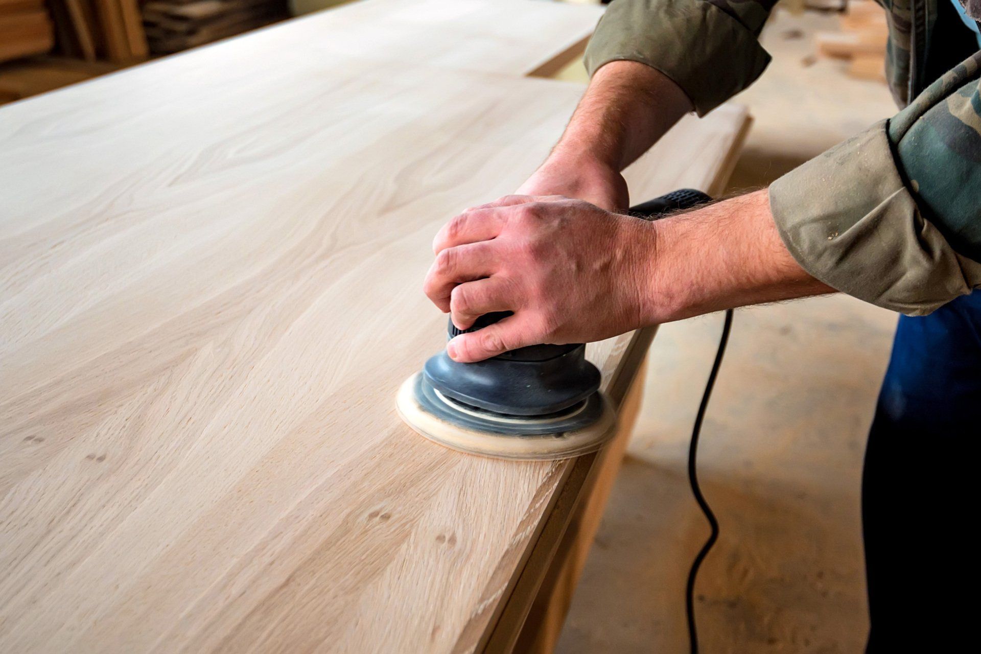 ébéniste qui sable dessus de table en bois avec outil électrique