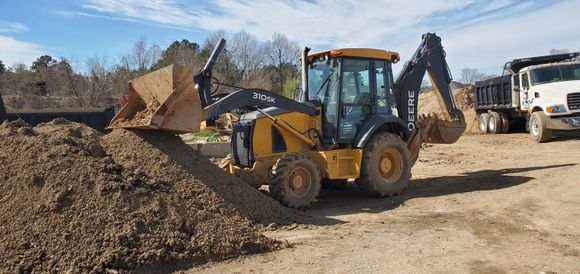Yellow backhoe loader moving dirt at a construction site under a clear blue sky.