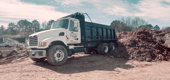 White dump truck loaded with soil at a dirt site, with piles of earth in the background