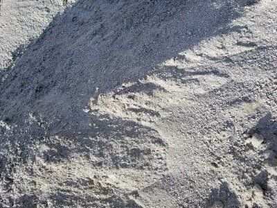 Close-up of gray gravel and sand with rough, uneven texture in sunlight