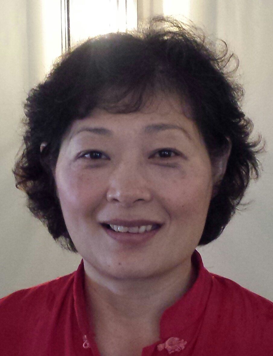Woman with dark hair, wearing a red shirt, smiling, indoors.